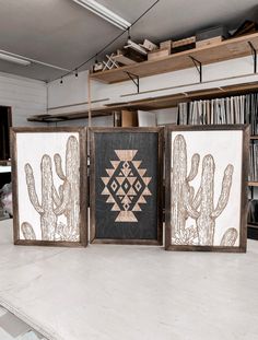 three framed art pieces with cactus designs on them in front of a bookshelf