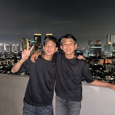 two young men standing next to each other in front of a cityscape at night