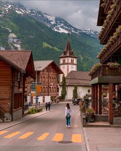 a woman is walking down the street in front of some buildings with mountains in the background