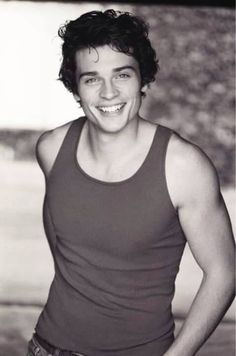 a black and white photo of a young man in tank top smiling at the camera