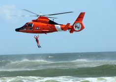 a red helicopter flying over the ocean with a person in it's arms and feet