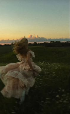 a woman in a pink dress running through a field at sunset with her hair blowing in the wind