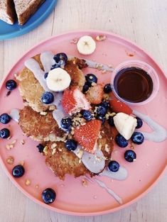 a pink plate topped with french toast covered in berries and blueberries next to a cup of coffee