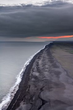 the beach is lined with black sand and water under a dark cloudy sky, as seen from above