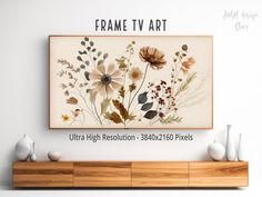 the frame tv art is mounted above a wooden cabinet with vases in front of it