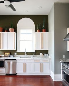 a kitchen with white cabinets and wood floors, an oven, dishwasher, stove and ceiling fan