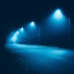 a person walking down a street at night in the fog with three lights on either side