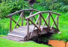 a small wooden bridge over a creek in a park with green grass and wildflowers