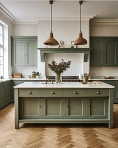 a large kitchen with green cabinets and wooden flooring, two hanging lights above the island