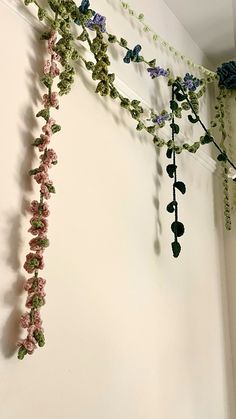 some flowers are hanging from the side of a white wall with green and pink vines