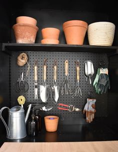 pots and gardening utensils are hanging on a pegboard