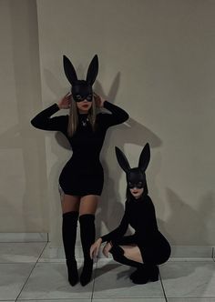 two women in bunny ears and black cats costumes posing for the camera with their hands on their head