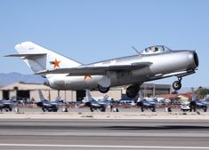 a silver fighter jet taking off from an airport runway with other planes in the background