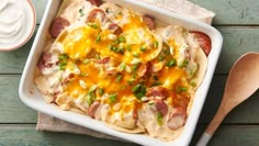 a casserole dish with sausage, cheese and green onions on it next to a wooden spoon