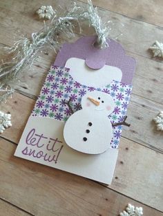 a snowman is on top of a purple and white gift tag that says let it snow