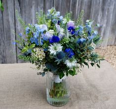 a glass vase filled with blue and white flowers on top of a burlock