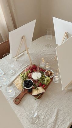 a table topped with cheese and fruit on top of a wooden cutting board next to two easers