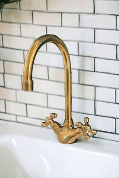 a gold faucet on the side of a white sink in front of a brick wall