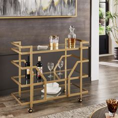 a gold bar cart with wine glasses and bottles on it in front of a painting