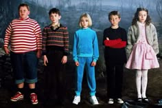 four young children standing in front of a wall with a painting on it's side