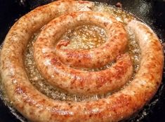 two sausages frying in a skillet on the stove top, with oil pouring over them