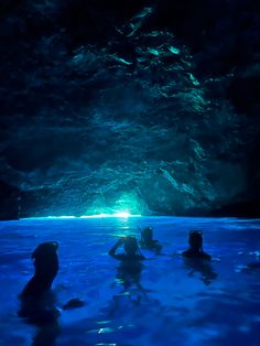 some people are swimming in the water near a rock formation at night with bright lights shining on them