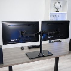 two computer monitors sitting on top of a wooden desk