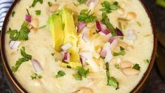 a bowl filled with soup and garnished with cilantro, red onion, avocado and lime