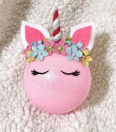 a pink unicorn ball with flowers on it's head is laying on a white blanket