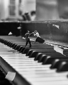 two figurines are standing on the piano keys