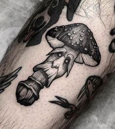 a man's leg with black ink tattoos on it, and mushrooms in the background