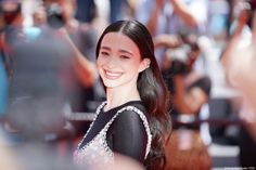 a woman with long black hair smiling at the camera and people taking pictures behind her