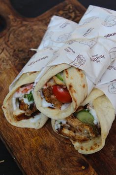 three burritos sitting on top of a cutting board with wrappers around them