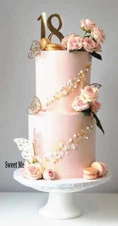 a three tiered cake with pink flowers and butterflies on top is decorated with gold numbers