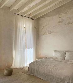 a white bed sitting in a bedroom next to a window with sheer curtains on it