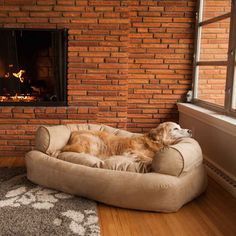 a dog is laying on his bed in front of the fireplace