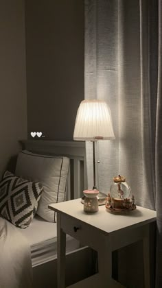 a small table with a lamp on it next to a bed