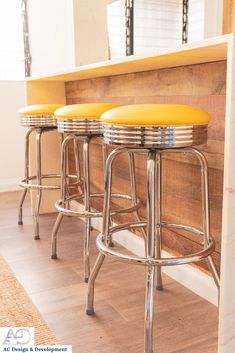 three yellow stools sitting in front of a wooden counter with metal barstools