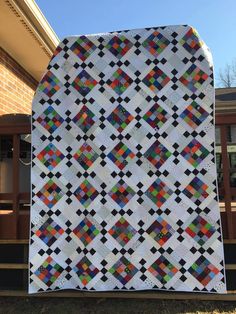 a white quilt with multicolored squares is on the ground in front of a house