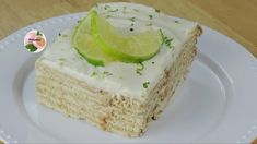 a white plate topped with a piece of cake covered in frosting and lime slices