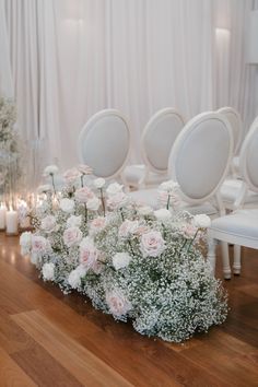 a bunch of white chairs sitting on top of a wooden floor next to flowers and candles