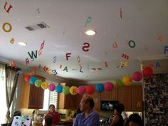 a group of people standing in a kitchen under a ceiling with letters and balloons hanging from the ceiling