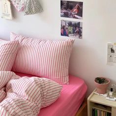 a bed with pink and white striped sheets, pillows and pictures on the wall above it