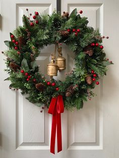 a christmas wreath with bells hanging on the front door, decorated with holly and red berries