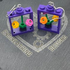 Unique Lego flower box in window drop earrings. Beautiful floral gift that will last for ever. Perfect as a fun gift or as a treat for yourself.Fun Floral Gift, perfect for Lego lovers, gardeners, botanists & horticulturists. The purple window frame has a Lego vase with 3 stalks and 3 flowers in pink, yellow and orange. The top stud, where the eyelet is screwed, isn’t fixed to the window, allowing you to position the window with the flowers at any angle you want.The Lego window measures 3.3cm lo Lego Vase, Lego Window, Lego Cards, Purple Window, Window Box Flowers, Daily Ideas, Lego Lovers