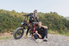 two people sitting on the ground next to a parked motorcycle with trees in the background