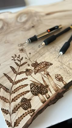 two pens are sitting on top of a wooden board with flowers and leaves drawn on it