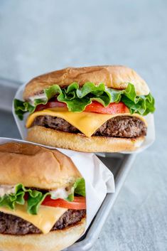 two cheeseburgers with lettuce and tomatoes on them sitting on a tray