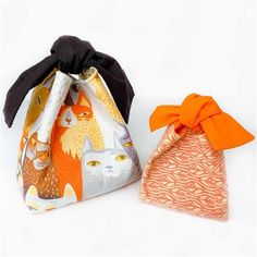 two bags with cats on them sitting next to each other, one has an orange bow