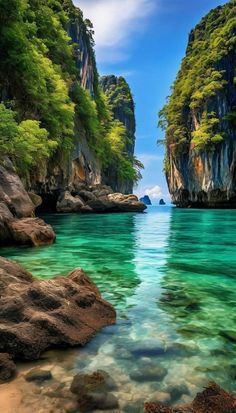 the water is crystal blue and clear with rocks on both sides, and green trees in the background